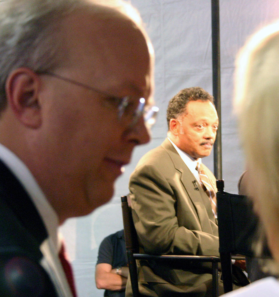 Karl Rove standing in the shadows while Rev. Jackson is interviewed on Fox News, reflective of their preferred roles in American